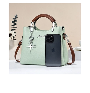 Detail of green pebble leather handbag with brown handles and star charm next to phone