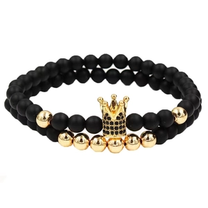 Detail of beaded bracelet with matte black beads and a gold crown charm with black stones