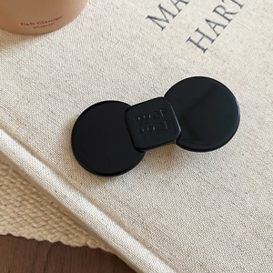 Close-up of a glossy black geometric hair clip with letter engraving on linen fabric