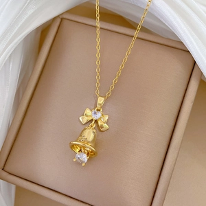 Close-up of a gold bow bell necklace with crystals on a beige jewelry box