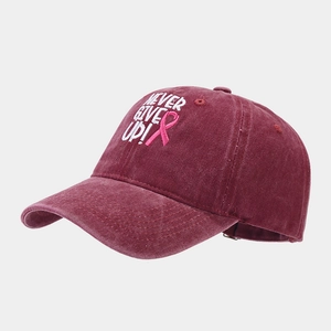 Détail de la broderie 'NEVER GIVE UP!' et ruban rose sur casquette bordeaux délavée