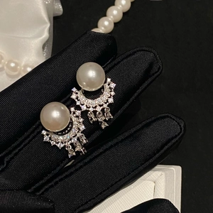 Detail of silver needle pearl tassel earrings with diamonds held in black silk gloves