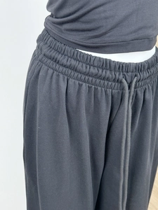 Detail of high-waist elastic waistband with matching drawstring on black wide-leg sweatpants
