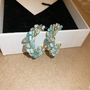 Detail of C-shaped hoop earrings with blue natural stones and gold metal beads