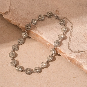 Macro shot of silver diamond-encrusted round cluster necklace on natural stone props