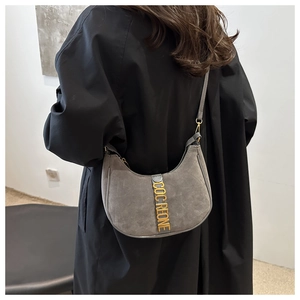 Détail du sac croissant en daim gris avec lettres dorées COCREONE et manteau noir