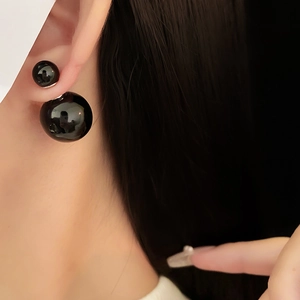 Detailed close-up of glossy black double-sided pearl stud earrings worn on ear