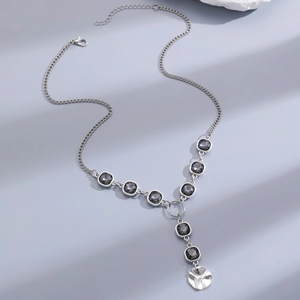 Detail of silver chain necklace with grey square stones and a round brushed metal pendant