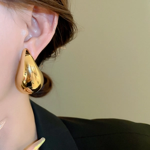 Close-up of a large golden teardrop earring with high-gloss finish worn on model