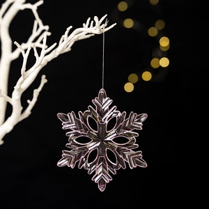 Macro shot of pink acrylic snowflake pendant on white branches with golden bokeh lights