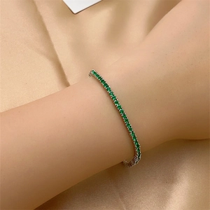 Close-up of a silver tennis bracelet with green zircon stones on champagne silk fabric