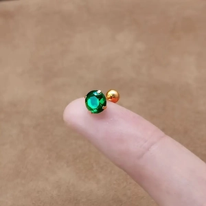 Detail of round green zircon stud earring with gold-plated screw back on fingertip