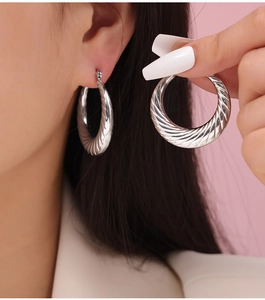 Detailed close-up of silver hoop earrings with a twisted spiral texture on a model