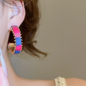 Close-up of woven C-shape earrings with pink and blue threads on gold metal edge