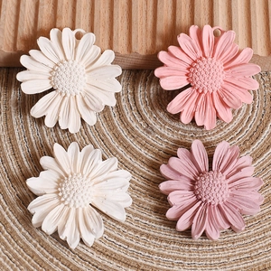 Detail of daisy flower resin pendants in white and pink tones on a straw mat background