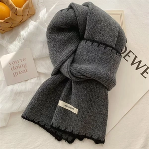Close-up of grey knit scarf folded on white surface with cozy lifestyle props