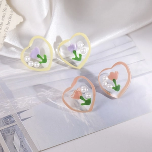 Detail of heart-shaped resin earrings with tulips and pearls on white silk