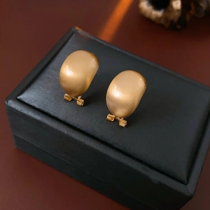 Macro view of matte gold oval C-shaped brushed earrings displayed on a black jewelry box