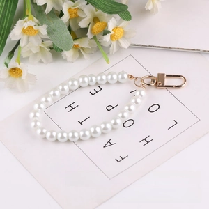 Close-up of white pearl phone charm strap with golden lobster clasp on decorative card
