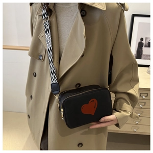 Fashionable black shoulder bag with red heart detail and geometric strap on a model
