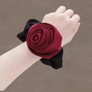 Detailed close-up of large burgundy fabric rose hair tie worn on the wrist by model
