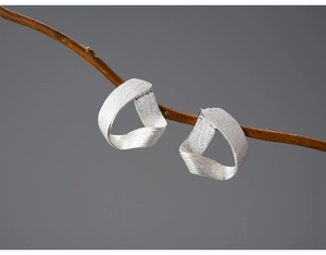 Macro shot of silver S925 triangular twisted earrings on a branch with matte finish