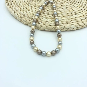Detail of multi-color pearl necklace with cream, silver, and bronze beads on woven mat