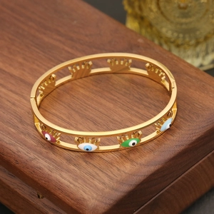 Golden evil eye bangle with colorful enamel charms on a dark wooden jewelry box