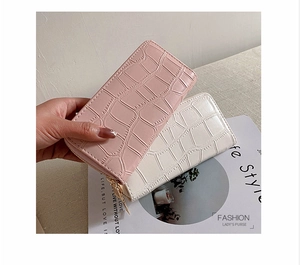 Detail of pink and beige faux crocodile leather wallets held by a model with a fashion magazine