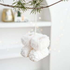 White plush mini Christmas boot ornaments hanging on a pine branch with warm bokeh