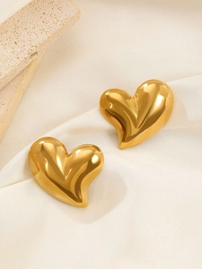 Macro shot of large 3D heart-shaped gold earrings with polished mirror finish on silk