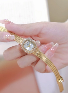 Close-up of gold square watch with rhinestone bezel and woven metal strap on wrist
