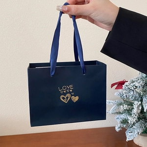 Detailed view of a dark blue gift bag with golden LOVE text and heart patterns held by hand