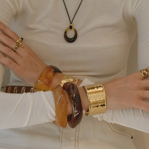 Primo piano di una modella che indossa bracciali in resina ambrata e metallo dorato