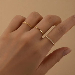 Detail of three thin gold stackable rings with chain and crystal designs on a hand model