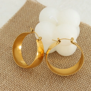 Polished 18K gold-plated wide hoop earrings on rustic linen with candle decor