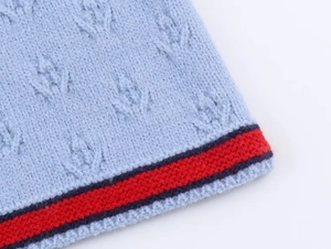 Close-up of light blue cable knit cardigan featuring red and blue striped hem detail
