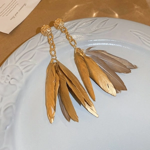 Vintage bohemian gold feather drop earrings on a decorative light blue ceramic plate
