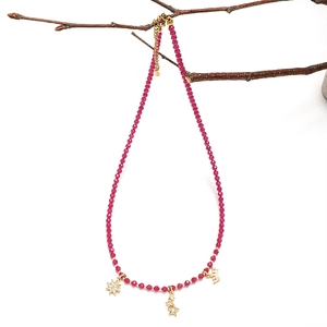Detail of fuchsia faceted beads and gold star pendants hanging on a wooden branch