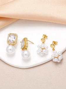 Detailed view of gold pearl earrings with square-cut gems and clustered pearls on silk fabric