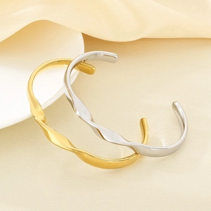 Close-up of gold and silver wave-shaped bangle bracelets on elegant neutral fabric