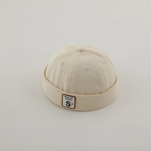 Dettaglio del berretto docker beige con trama in tela e toppa in pelle con lettera S