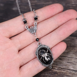 Silver bat necklace with black gemstone and spider pendant held by hand in natural light