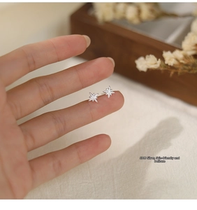 Detail of small S999 sterling silver eight-pointed star stud earrings on a fingertip