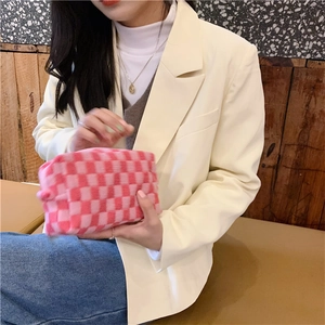Detail of pink and red checkered knit makeup bag held against a minimal background