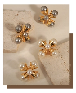 Close-up of elegant cross-shaped earrings with white and grey pearls on gold base