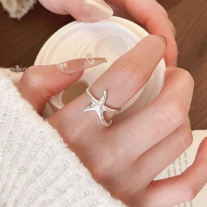 Close-up of a matte silver starfish open ring worn by a model in a cozy scene