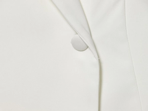 Detailed close-up of a white woven fabric blazer featuring a matching covered round button