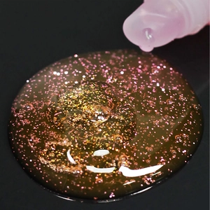 Glossy dual-layer rainbow lip gloss tube with shimmering golden and pink glitter particles