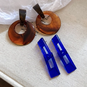 Detail of amber resin hoop and transparent blue geometric drop earrings on texture